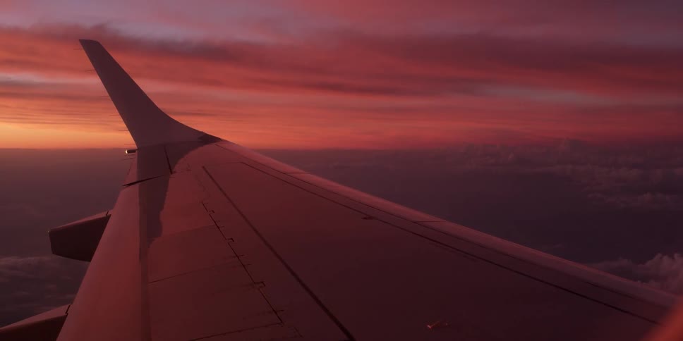 A plane wing high in the air at sunset