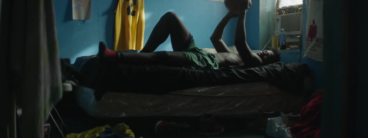A man lays down on a bed throwing a basketball up
