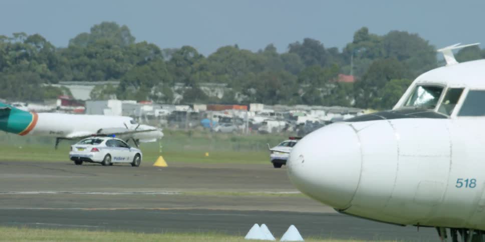 Cars driving on the pavement in an airport with a parked plane nearby