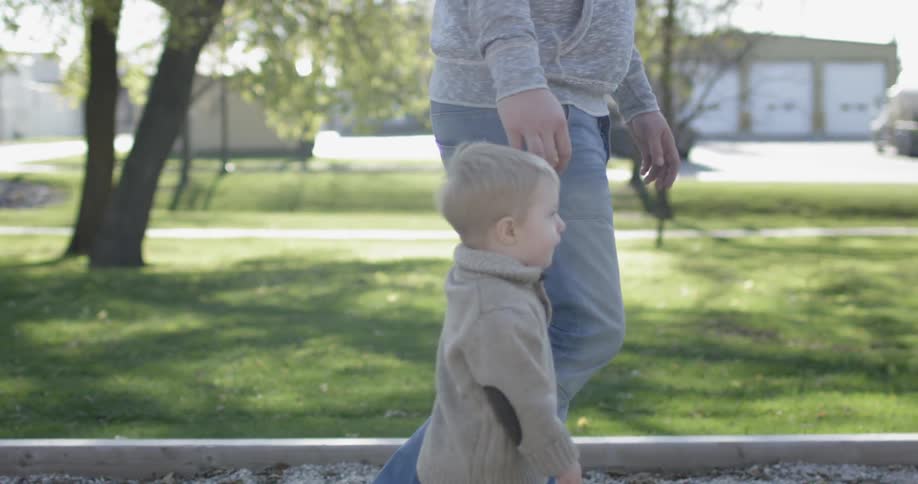 A young child walks on a playground holding the hand of his parent