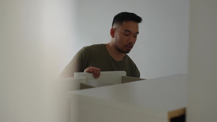 Two men take apart a dresser in an apartment