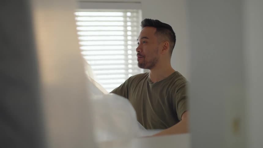 Young man wrapping furniture at home with large sheets of translucent plastic