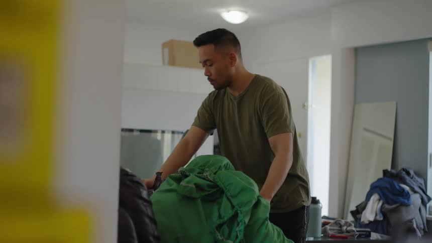 Man doing chores at home carries bags of laundry and puts them on a couch in the living room
