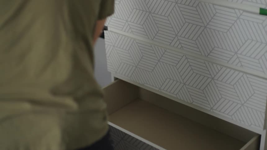 A man is standing near a dresser taking clothes from a drawer and putting them into a laundry bag