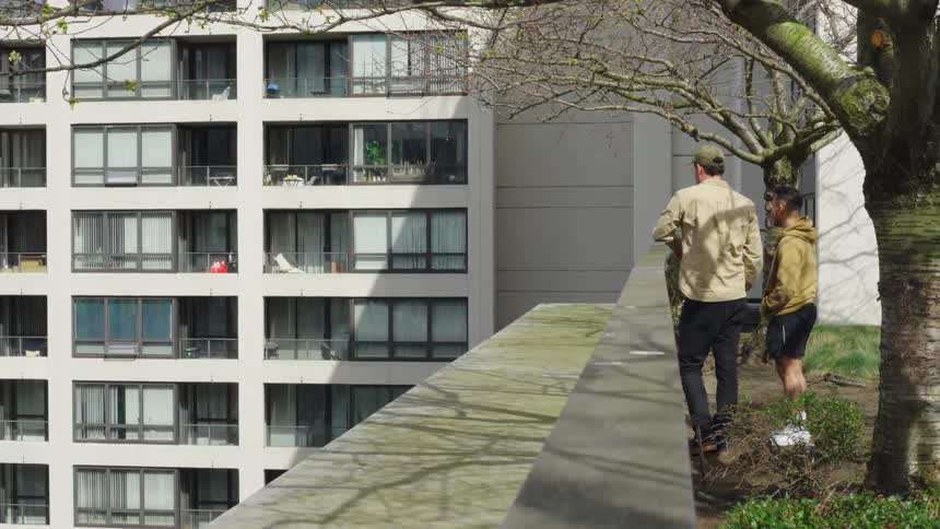 Two men standing on the garden on a roof of a building looking at an apartment building