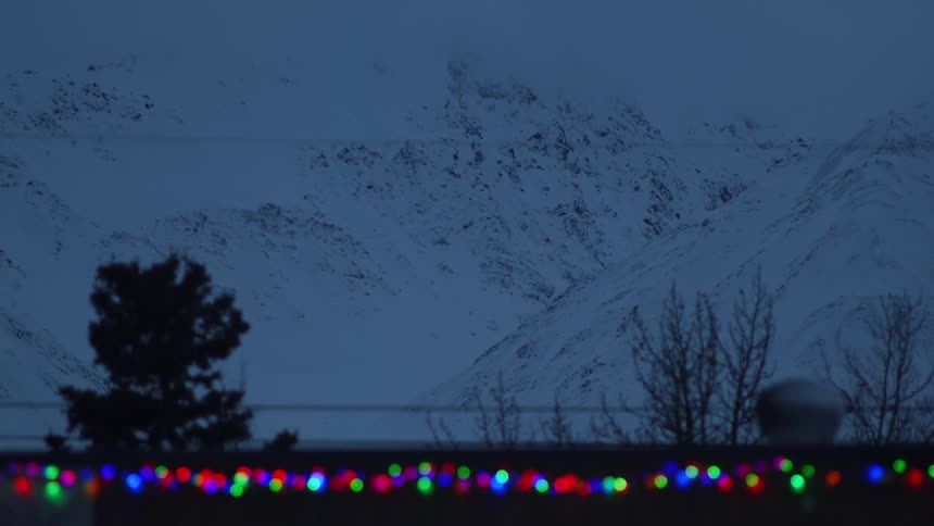 Snow covered mountains in the distance and multi colored lights on an outdoors railing flashing