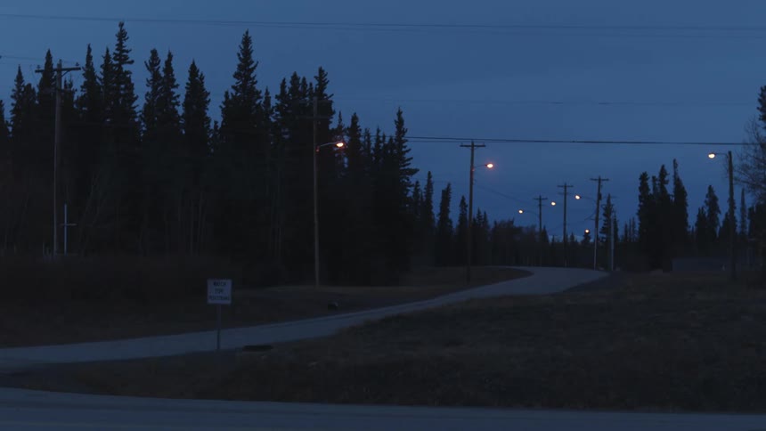 A vehicle pulling a boat drives down a rural road past a forest