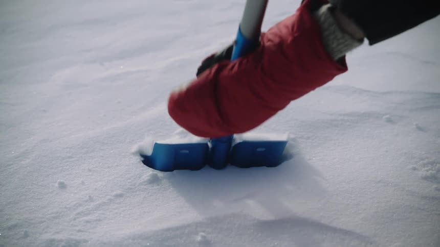Snow covered ground as a person using a shovel shovels the snow from the areea
