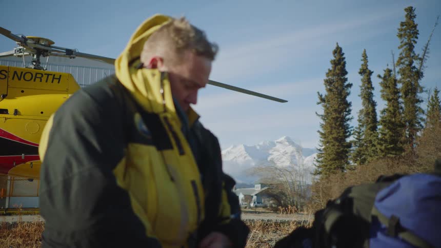 Man standing near a helicopter on a helipad in the mountains wears a thick jacket