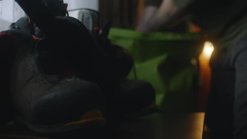 A green bag that a man walks over and gets into pulling out boots and other equipment