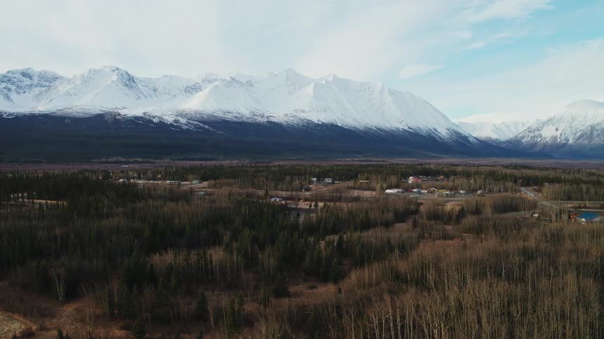 An aerial shot of a snowy mountain range behind a forest in winter