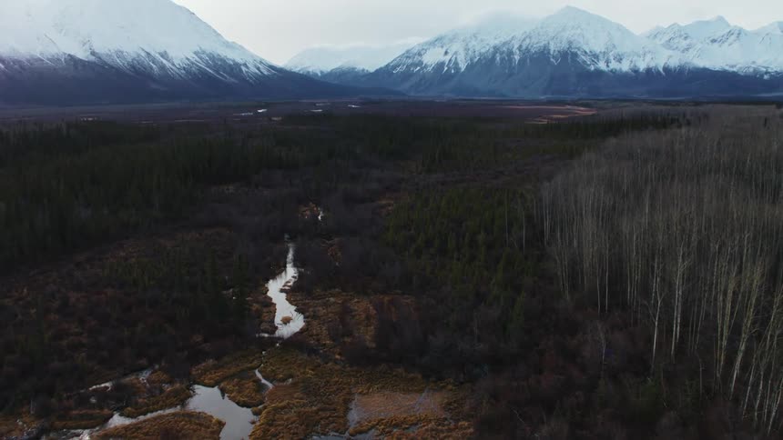 An aerial view of a plains marshland and stream leading to a distant snowcapped mountain range
