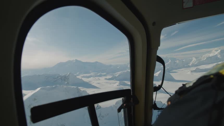 Aircraft flies over snow covered terrain dotted by mountains on a sunny day