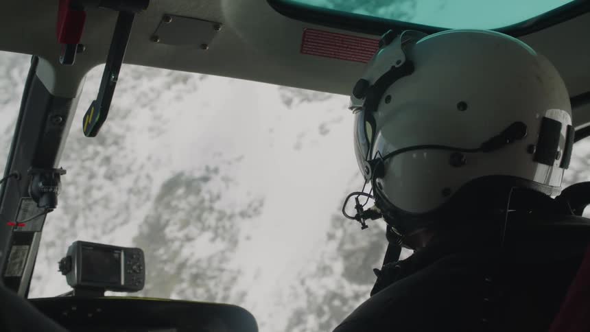 A pilot in the cockpit of an aircraft looks ahead as he flies near snow covered mountains