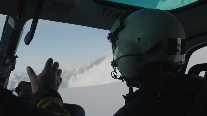 Pilots fly helicopter over snowy mountains
