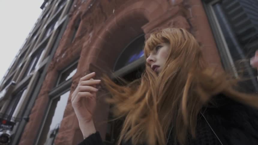 A woman standing in front of a building runs her hands through her hair
