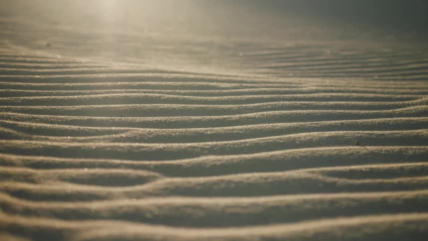 The sun shines brightly upon ripples and wave patterns in the desert sand