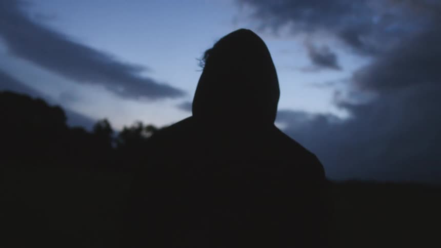 Silhouette of a hooded person walking in the countryside at nightfall