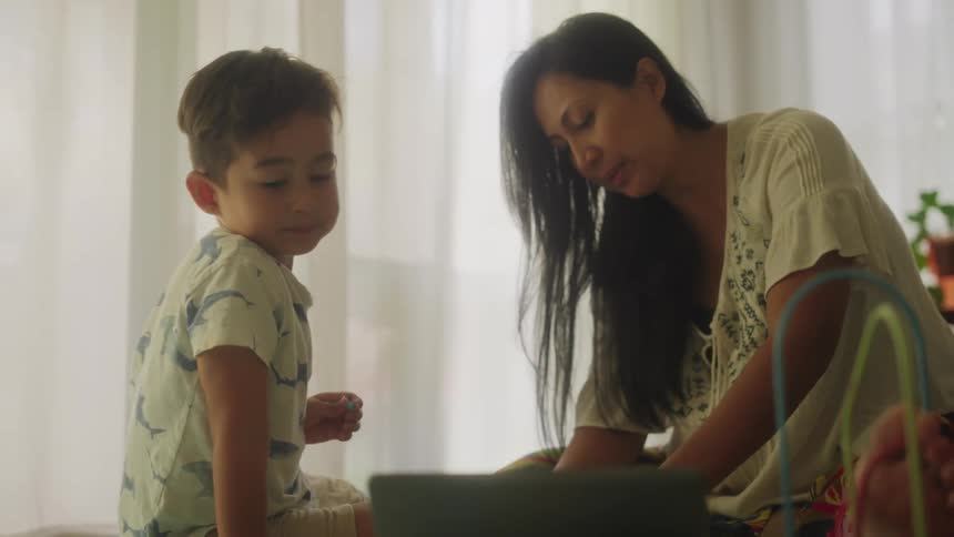 Boy interacts with mom but mostly pays attention to computer screen