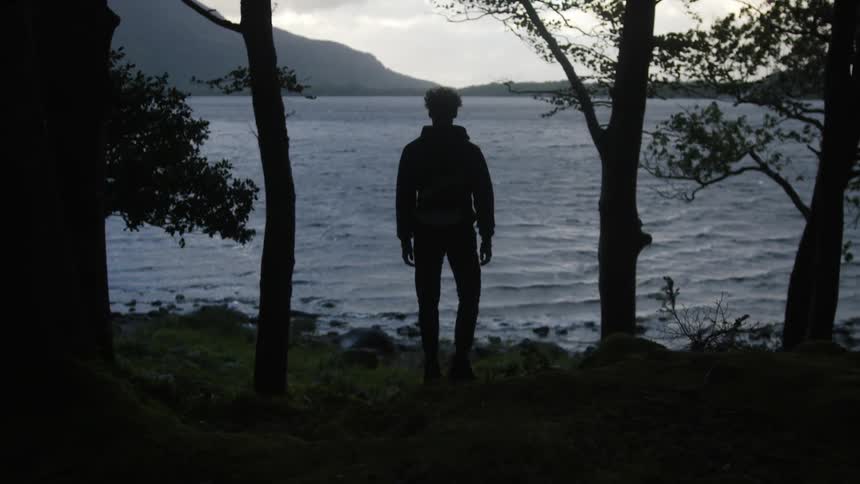 Silhouette of a young man looking at a lake in the mountains at evening