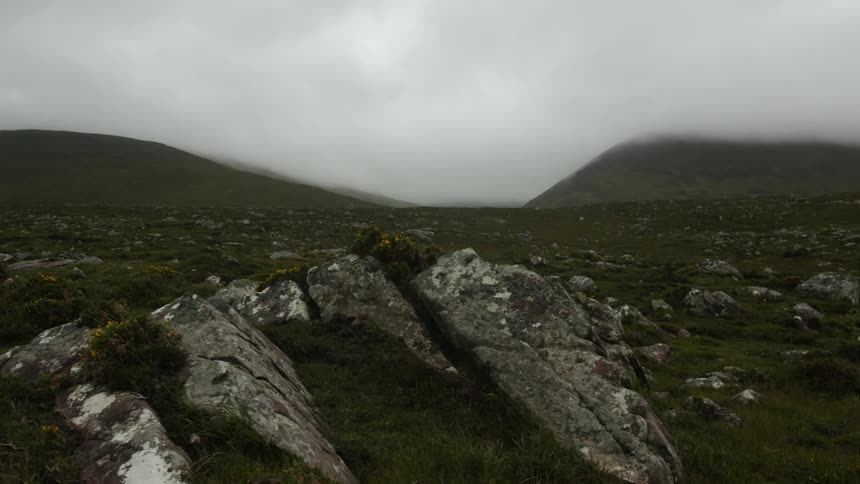 View of a rocky mountain top and pasture surrounded by clouds on a rainy day