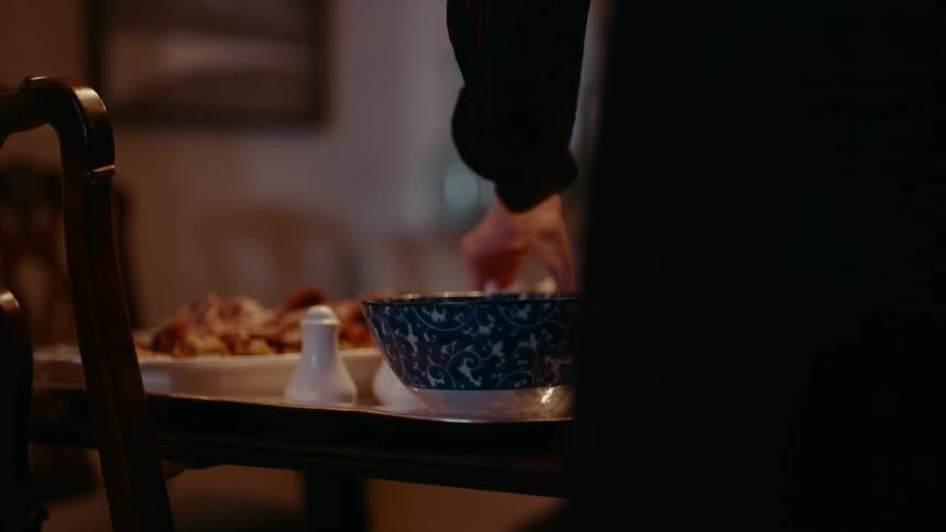 Headlights from outside play across woman setting food on tray on table