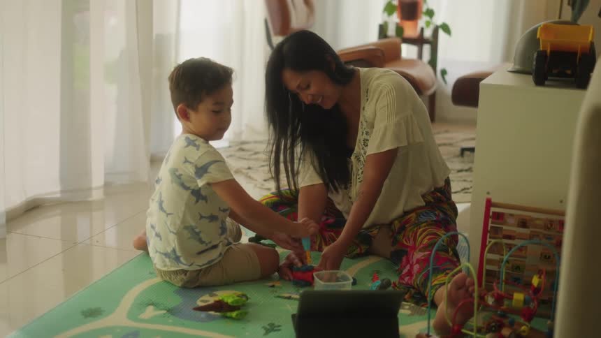 Son and mother sitting on the floor play with toys