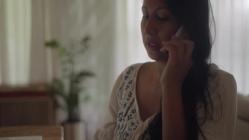 Pregnant woman sitting at the table talking on the phone takes notes on a notebook