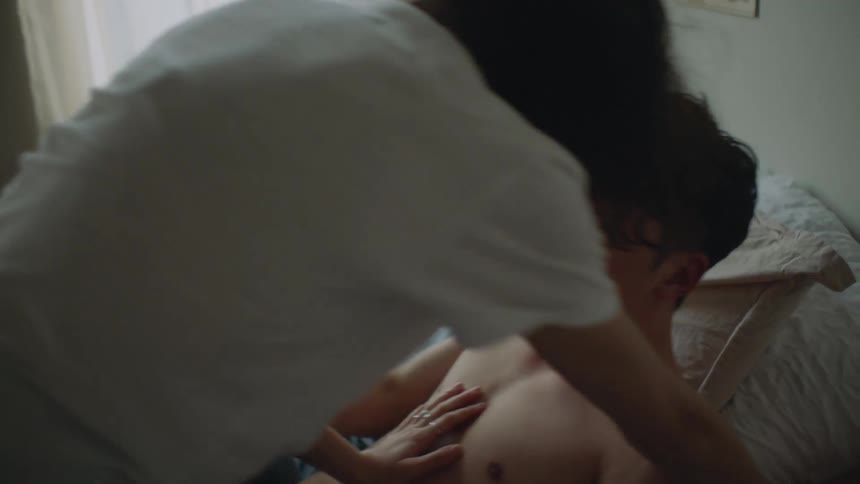 Topless man and woman with white shirt and jeans make out on bed in bedroom