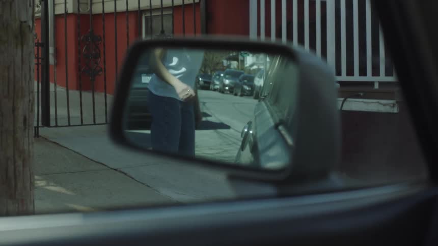 Close up of person closing a car door and walking away reflected on the rearview mirror