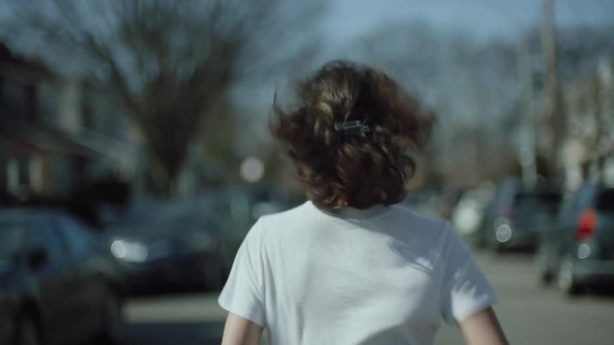 The backside of a woman running down a road with cars parked on either side