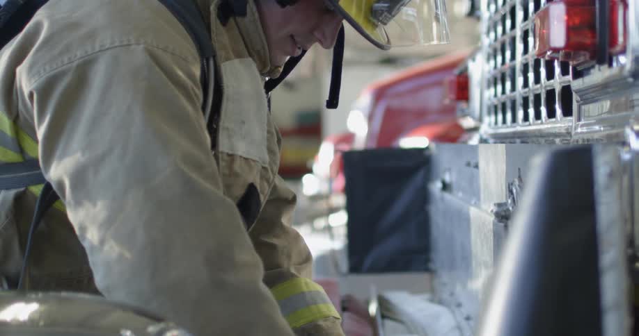 A firefighter in full gear is putting away a folded up firehose
