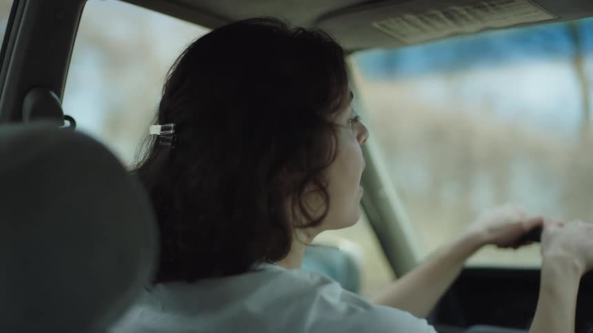Woman with dark hair and white t shirt drives car