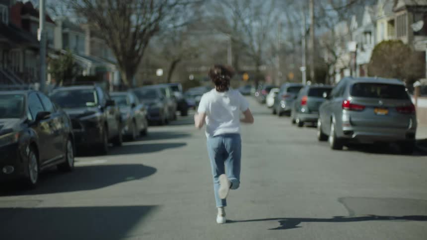 A woman runs down a neighborhood street with cars parked on either side