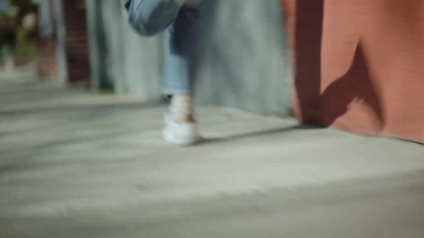 Woman with jeans and a pair of white shoes runs on sidewalk in the street