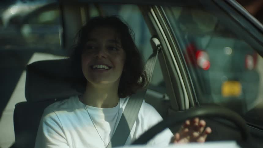 A teenage girl is talking as she drives an automobile through a neighborhood