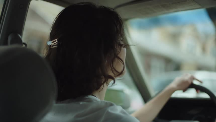 A teenage girl is talking as she drives an automobile through a neighborhood