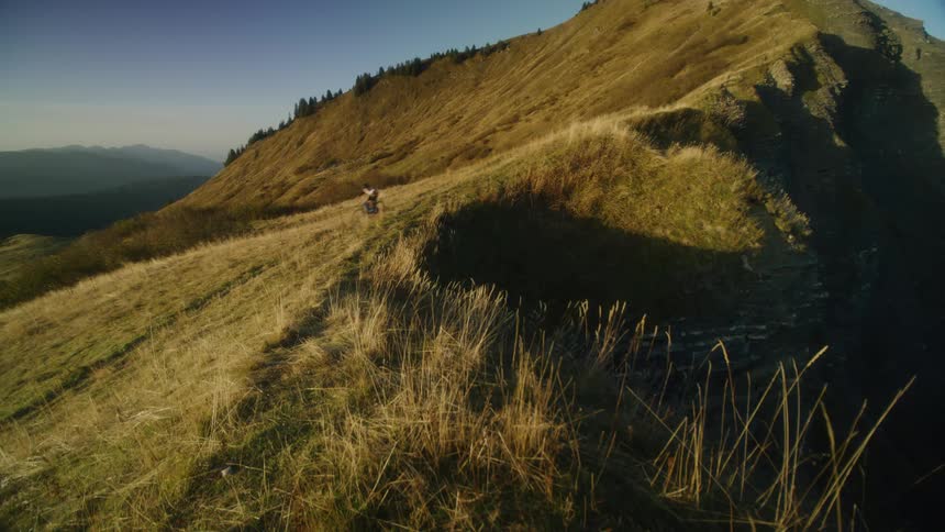 A grassy hillside of a mountain as a person rides their bike down it