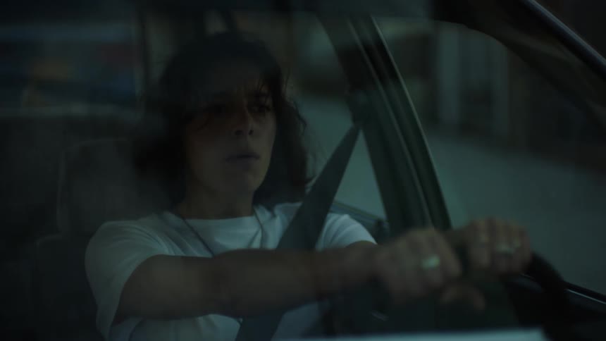 A teenage girl is talking as she drives an automobile through a neighborhood and stops in a garage