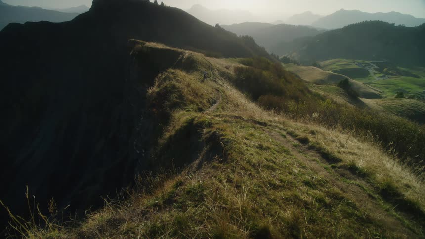 Mountain ranges with trails along the ridges as a person on a bicycle rides along the path