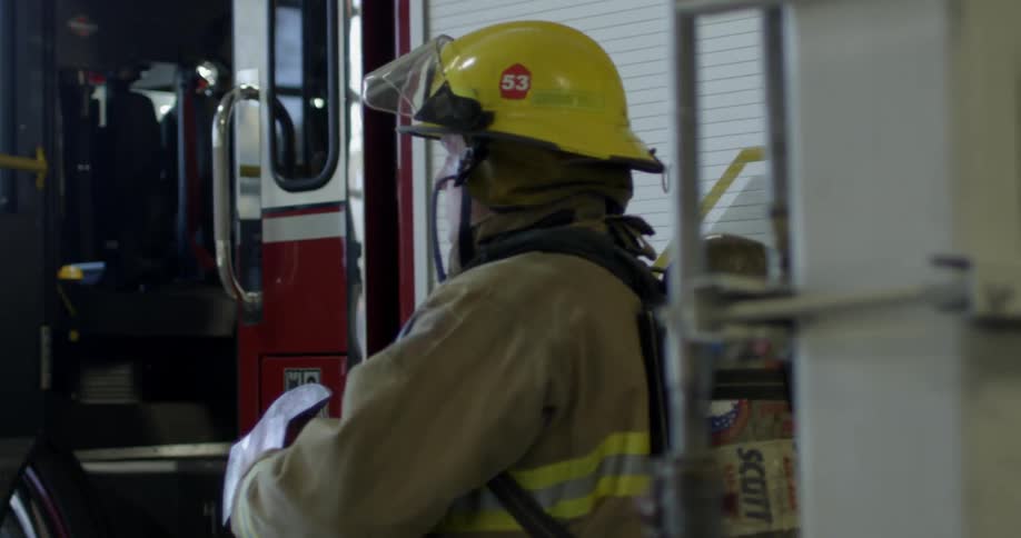 A firefighter takes an axe from a fire-truck then walks away
