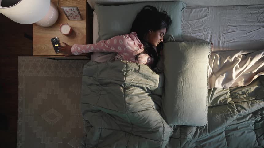 Woman sleeping in bed reaches for alarm on smartphone then gets out of bed