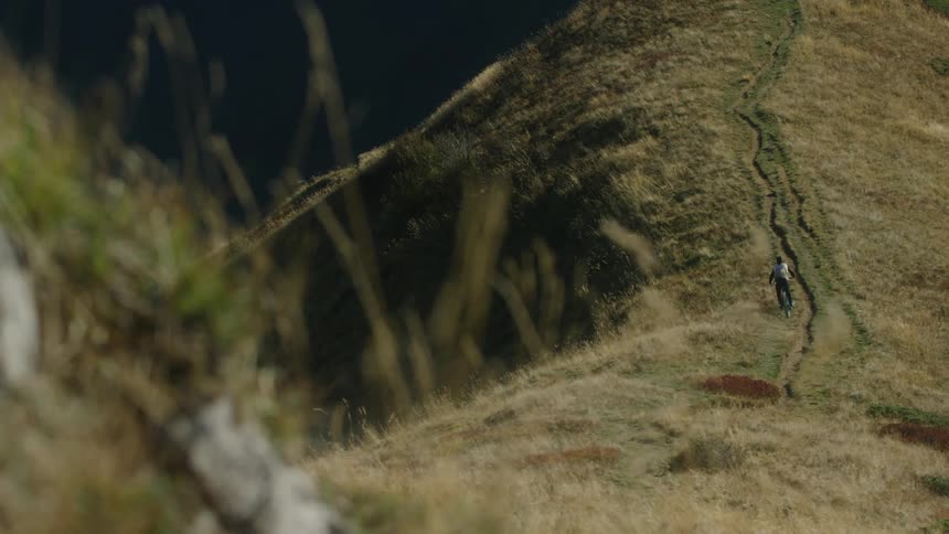 Cyclist rides along trail up sloping grass covered mountain