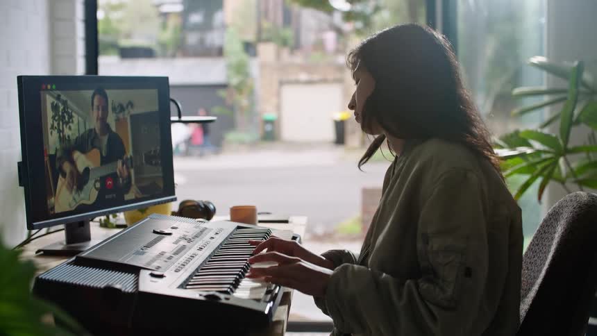 A woman plays a musical keyboard while participating in a video chat with a man playing the guitar