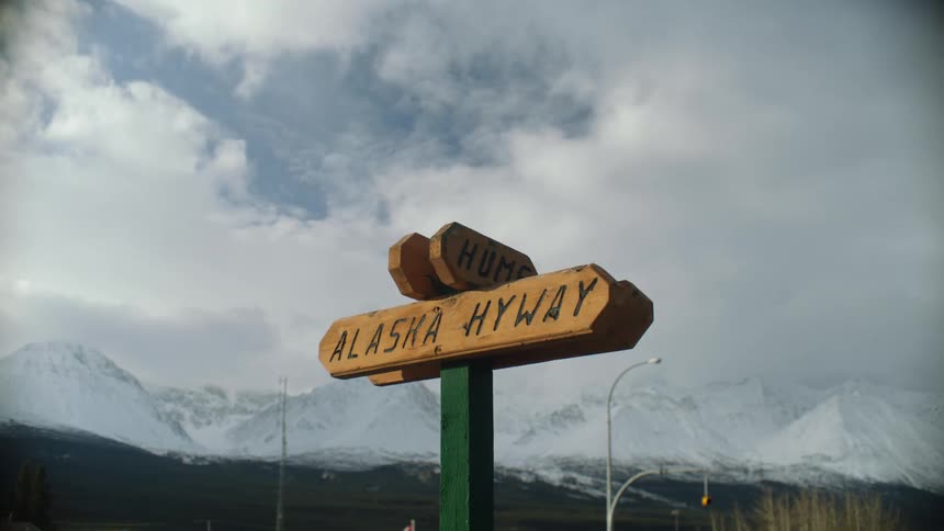 A wooden road sign and snow covered mountains in the background