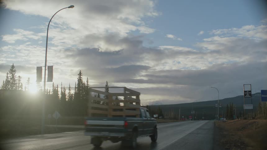 Sparse traffic flows along highway as sun shines through conifers in woods