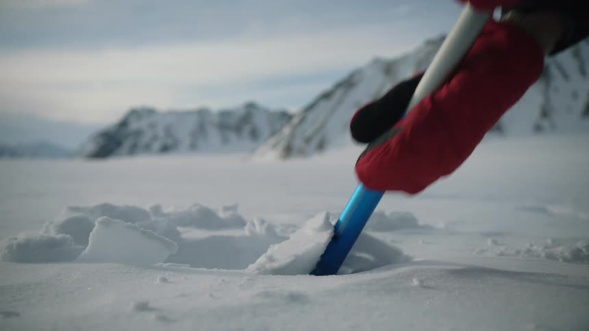 A person wearing red gloves shovels snow with mountains in the background