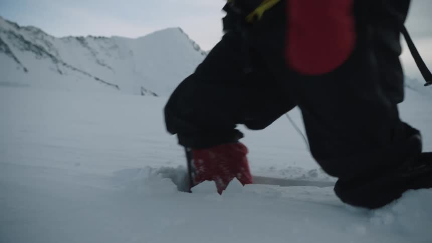 A person in cold weather clothing struggles to walk through deep snow in the wilderness during the day
