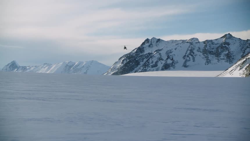 Helicopter flying over snowy field and mountains