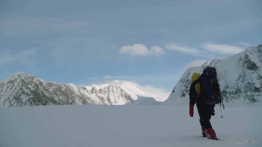 Man with yellow coat red gloves and black pants hikes through snow on the mountain